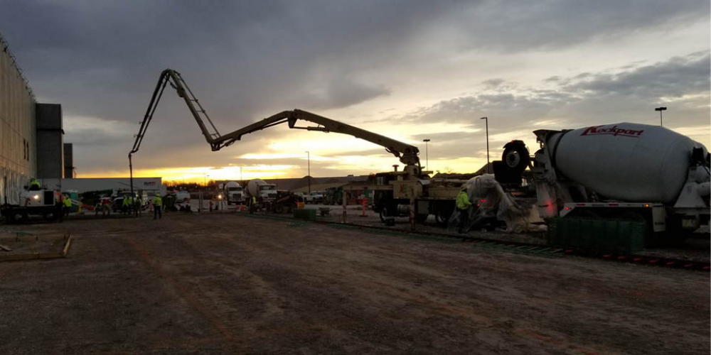 A construction site at sun set with various equipment and crew throughout the photo.