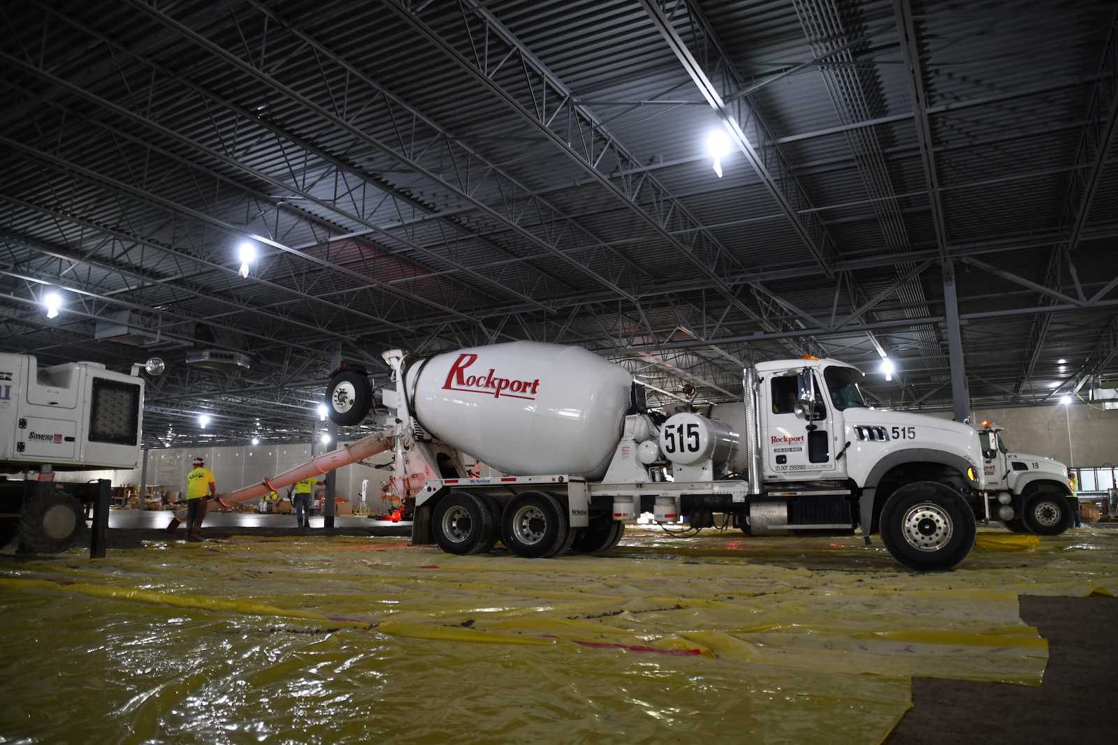 White cement truck with red Rockport logo on side dispensing concrete in warehouse building.