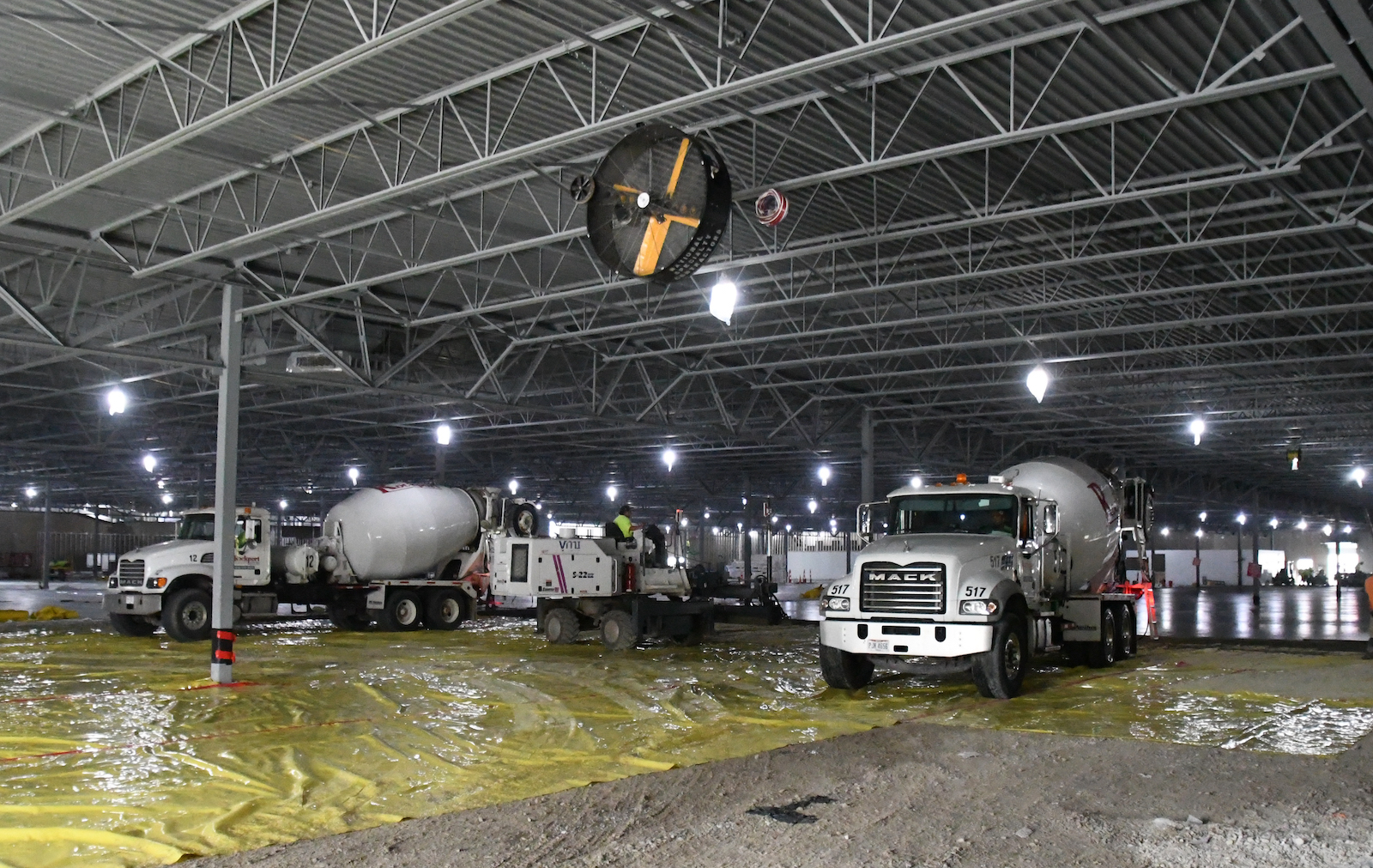 Concrete trucks are pointed towards camera during the pouring of concrete inside large building.