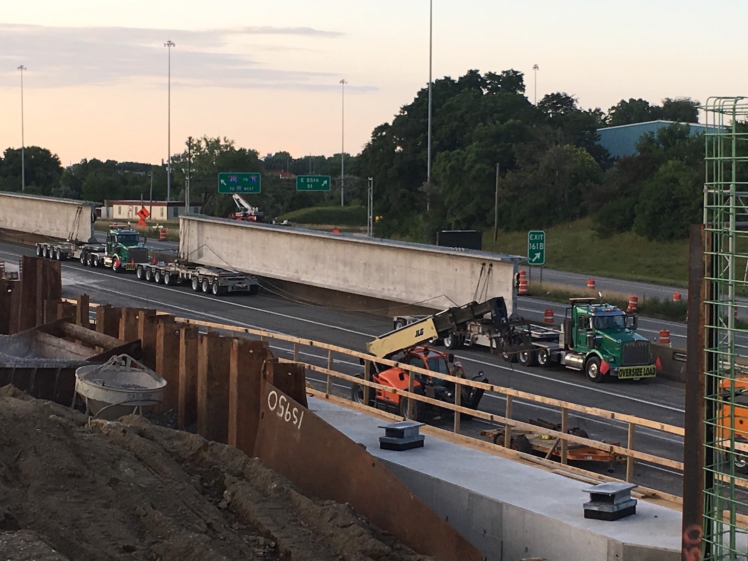 With the sun kind of set, two semis move large pieces of concrete for bridge construction.