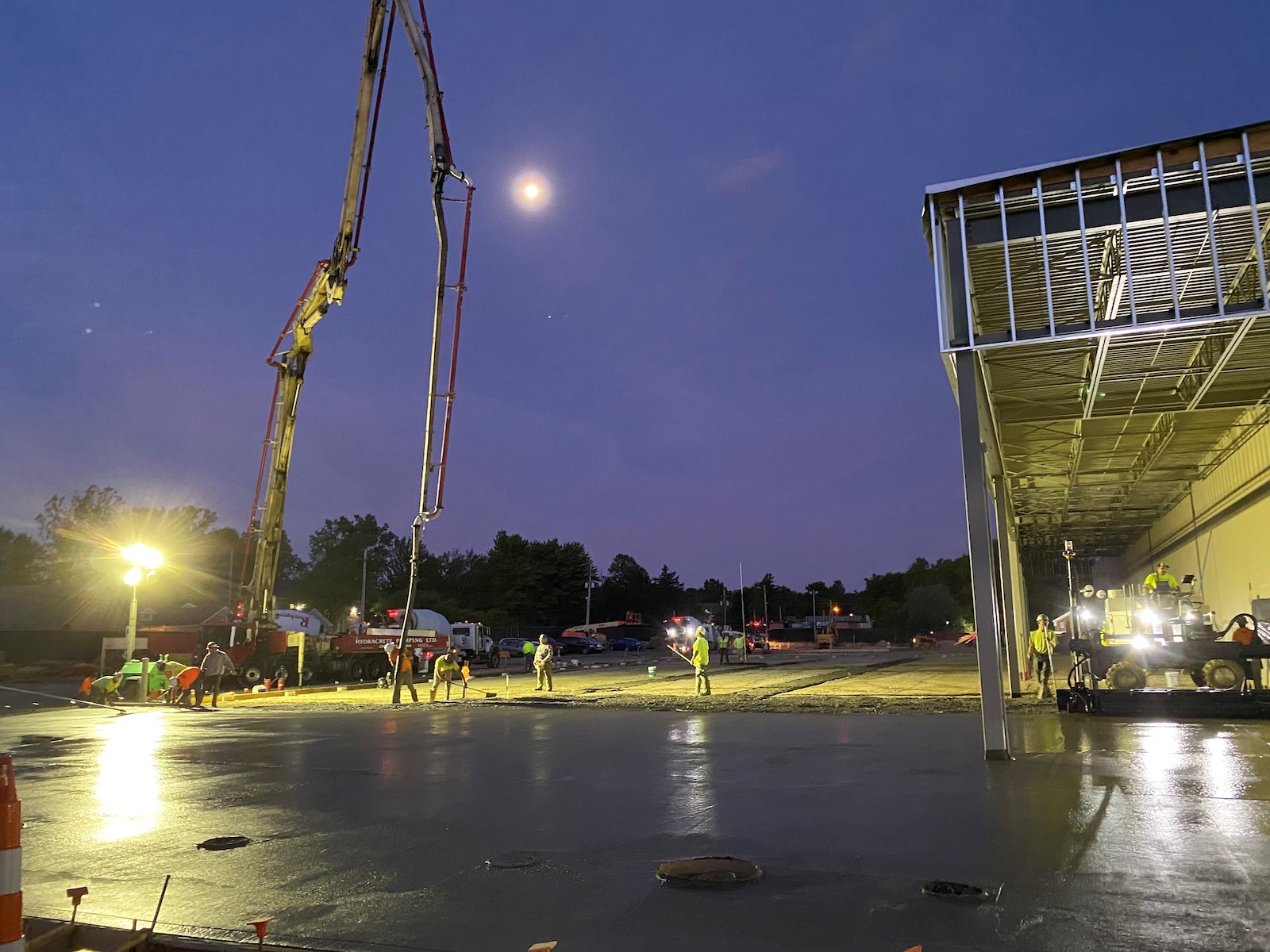 Construction workers continue to pour concrete as the sun sets with the help of several portable lights.