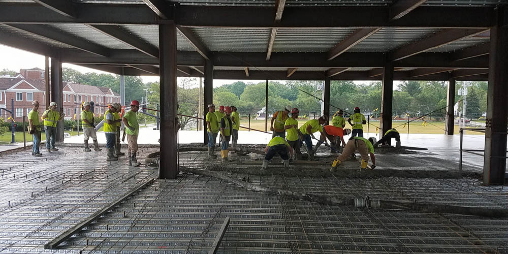 Large group of constructions works hold tools as they level concrete under building framing.